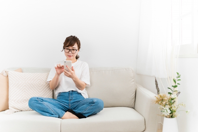 ソファーでくつろぎながらスマホを見る女性